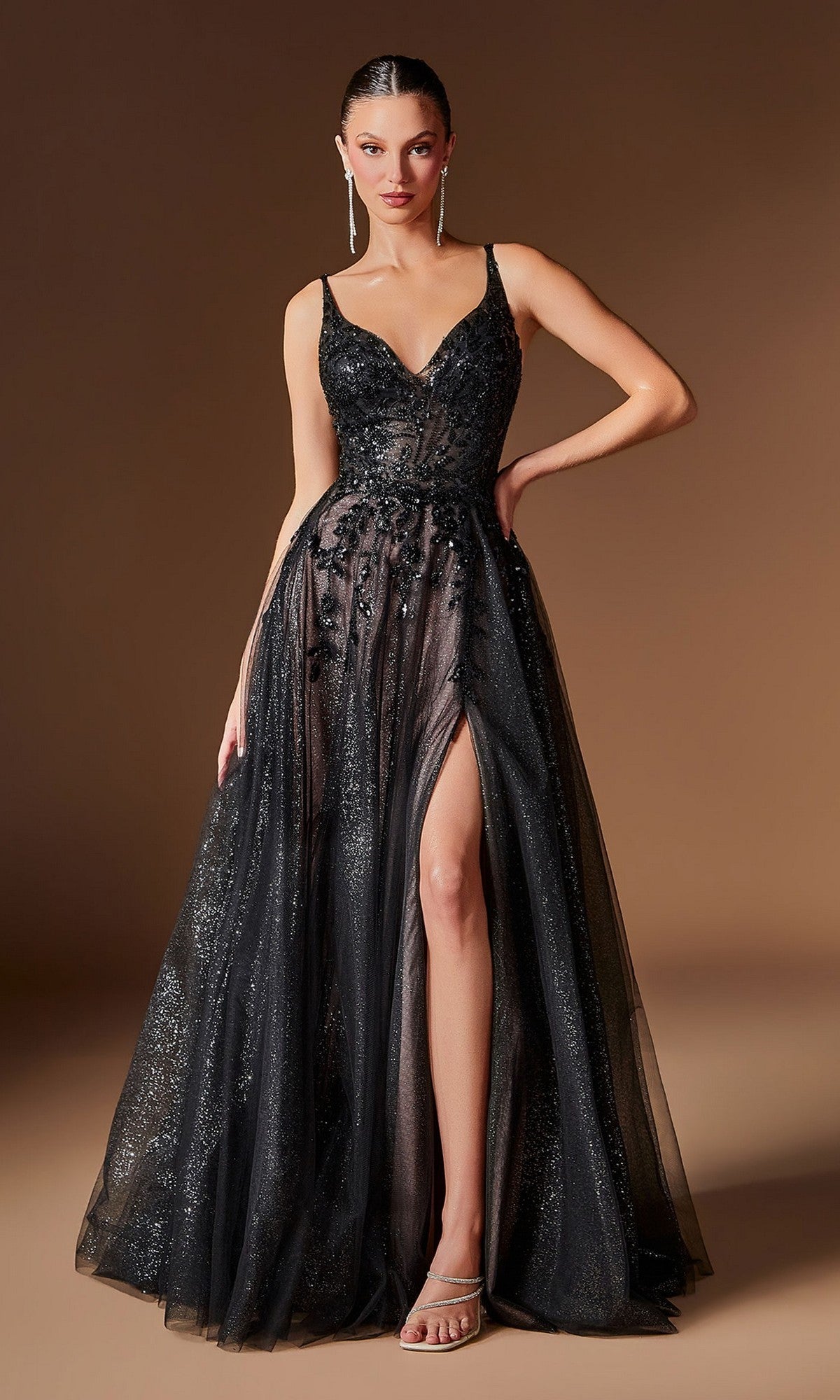 A woman stands against a plain brown background wearing the Ladivine CD2412 long prom dress in Black/Nude, featuring a sleeveless design, deep neckline, beaded embellishments, glitter tulle a-line skirt with sheer overlay and high slit.